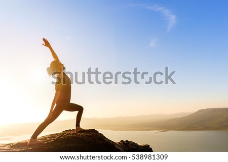 young asian woman practicing yoga warrior pose at sunset. Zen wellness and wellbeing concept.
