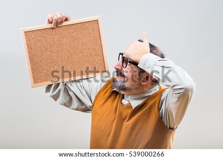 Nerdy businessman is worried because of something while holding empty cork board.
Worried nerdy businessman with empty cork board