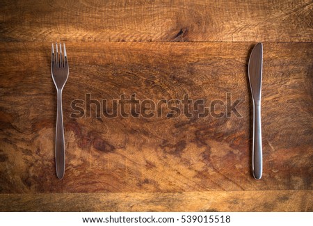 Knife and fork with missing plate on wooden table, top view Royalty-Free Stock Photo #539015518