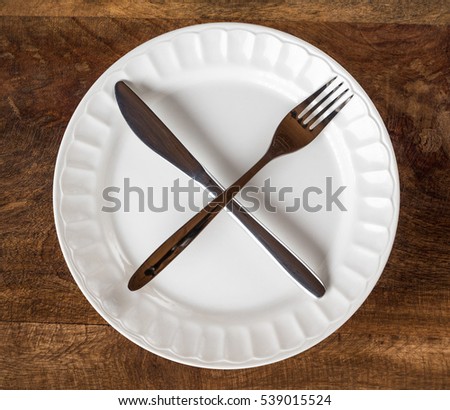 Intermittent fasting concept with knife and fork showing cross symbol on white plate against wooden table, top view Royalty-Free Stock Photo #539015524