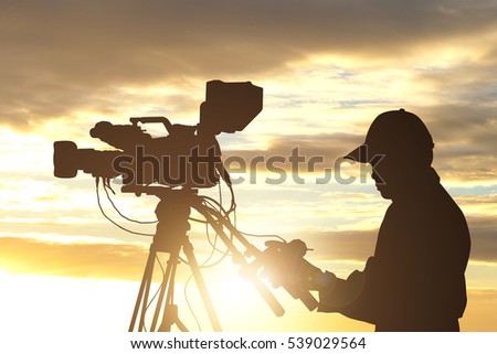 Silhouettes of video camera man operator against sunrise sky