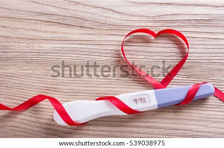 Pregnancy test positive with two stripes, a gift with a red ribbon and bow in the shape of a heart. Plastic cover on wooden boards. I am pregnant