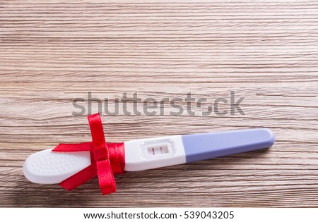 Pregnancy test positive with two stripes, a gift with a red ribbon and bow. Plastic cover on wooden boards. I am pregnant