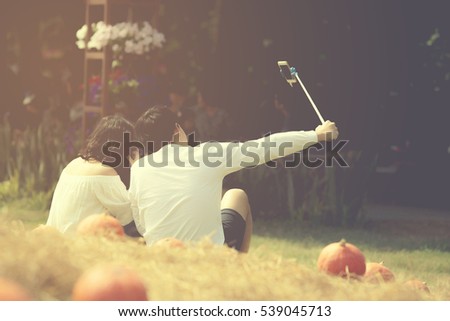 technology, summer holidays, couple man and woman sitting taking picture by smartphone selfie stick in garden fields.