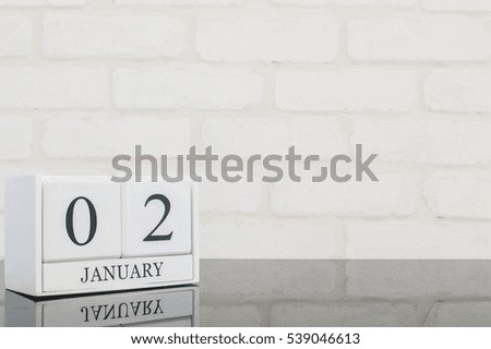 Closeup white wooden calendar with black 2 january word on black glass table and white brick wall textured background with copy space , selective focus at the calendar
