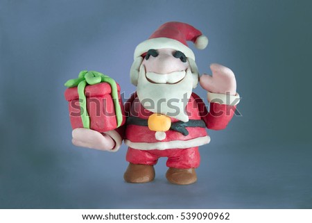 Cute Santa Claus with red gift box on right hand and waving left hand made out of play dough in grey background