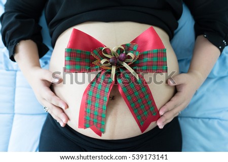 Pregnancy photo with bow on the bed. Maternity Photography with prop. A new year gift. A christmas gift. Selective focus at bow.  