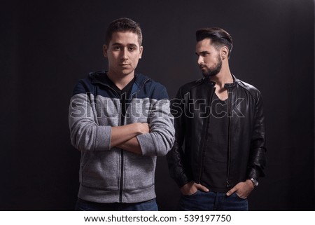 Two young adult men, posing, casual clothes. Black background, studio.