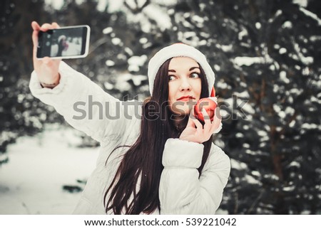 Girl taking selfie. Christmas girl outdoor self portrait. Woman in winter clothes and claus hat on a snow field