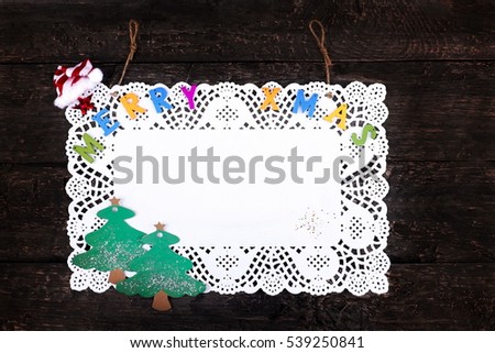 Merry Xmas greeting text written with small, colorful, wooden letters on a pure white napkin, placed on a wooden, vintage look background- Top view