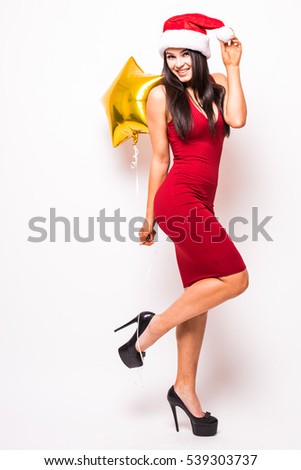 Pretty young woman in red dress and santa christmas hat with gold star shaped balloon smiling over white background
