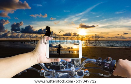 Man using a cell phone while riding a motorcycle, blur image of sunset on the beach in Phuket, Thailand as background.