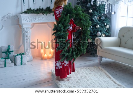 woman with a Christmas wreath in the hands in the living room with Christmas decorations, gifts, candles, firtree, toys