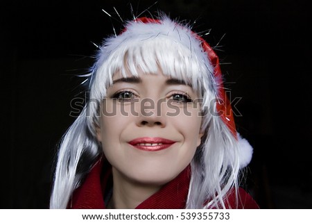 Photo of a woman on a dark background. The woman - a cap of Santa Claus with blonde hair. The woman is full-face, she smiles. White, red, black colors.