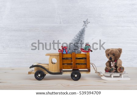 Christmas background with toys-wooden truck carries a teddy bear, Christmas tree, decorations and gifts. White and silver wood background as a backdrop