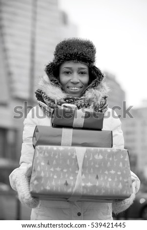 Portrait of happy woman carrying stacked gifts during winter