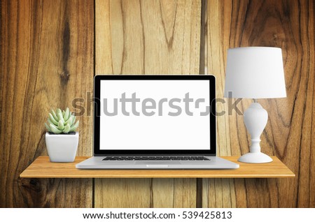 Laptop, lamps and potted cactus on bookshelf in the wall, with blank screen.