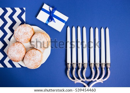 Celebration of Hanukkah. Candlestick with fried donuts, gift, on white and blue background, top view