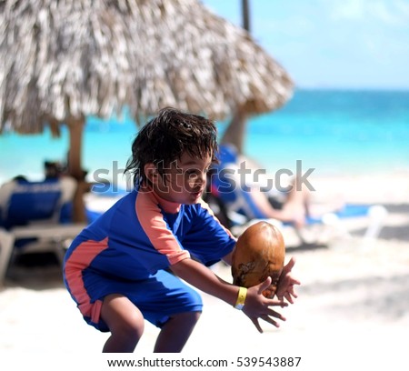 Little boy in swimming suit playing with coconut on a tropical beach