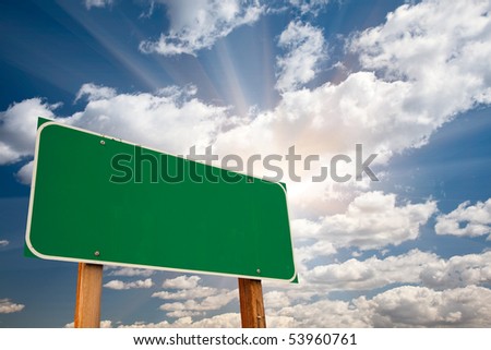 Blank Green Road Sign over Dramatic Blue Sky with Clouds and Sunburst - Ready for your own message and Room For Copy on Clouds.