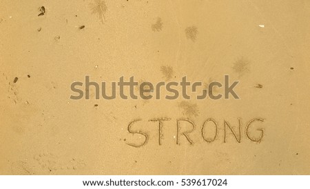 Handwriting words "STRONG" on sand of beach