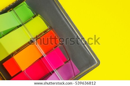 Top angle of colorful self stick notes in a black case against a yellow background