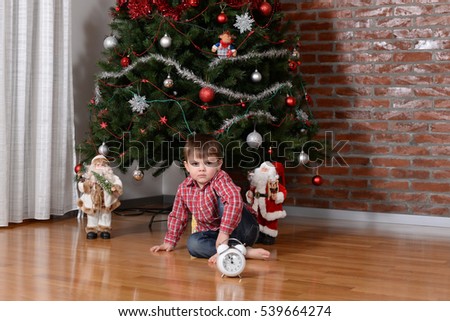 Five minutes to midnight, the boy waiting for New Year and Santa Claus under a Christmas tree