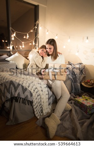 Beautiful mother and daughter opening a magical Christmas gift in the cozy interior of the house. New year.
