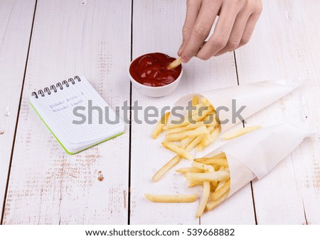 Teenager is dipping french fries potatoes into tomato ketchup on white wooden table. Selective focus.