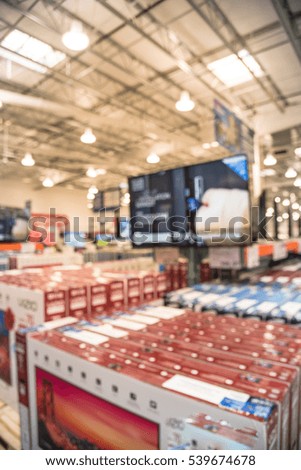 Electronic department store with bokeh blurred background. Television retail shop, TVs display on shelf at wholesale store. Defocused warehouse interior technology aisle and shelves. Business concept.