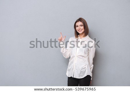 Portrait of a smiling girl in shirt pointing finger up and looking at camera over white background