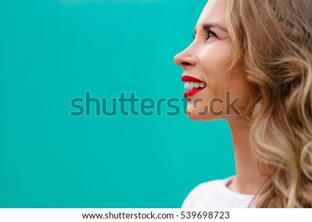 Close up portrait of pretty young happy woman with red lips make-up against green wall.