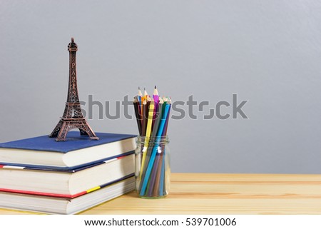 Eiffel tower statue and stack of books ,color pencils on the school desk, knowledge/education concept, with empty space  