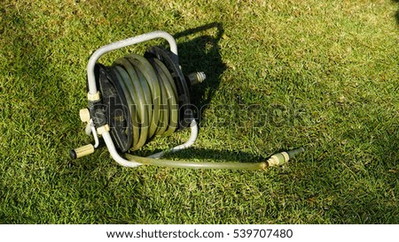 The old watering rubber pipe for gardening was rolled in the white wheel reel equipment for tidy, put on the green grass lawn field in the backyard