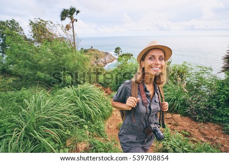 Traveling and photography. Young woman with camera and backpack walking on mountains near the sea.