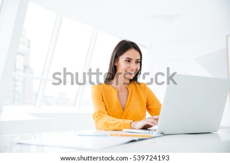 Business woman in orange shirt using laptop computer and sitting by the table in office