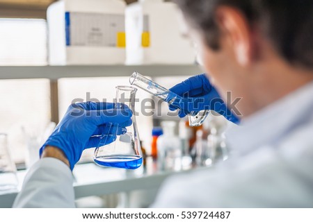 Male medical or scientific laboratory researcher performs tests with blue liquid. Close up Royalty-Free Stock Photo #539724487