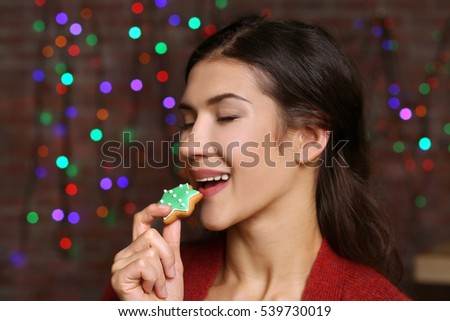 Pretty young woman with tasty Christmas cookie against defocused lights, close up