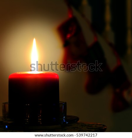 Burning red candle against dark background with silhouettes of Christmas stockings