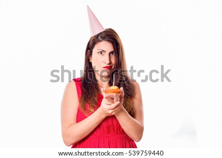 A young woman with a birthday cap and holding a cupcake isolated on white background