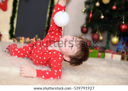 Little boy in New Year's pajama play with snowball in front of fireplace