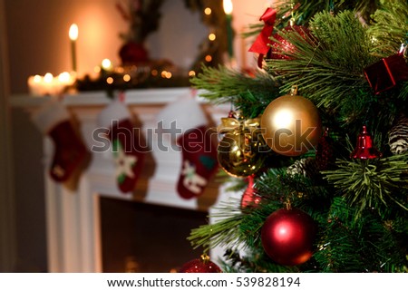 Beautiful decorated fireplace and Christmas tree at cottage. A rich christmas tree with lots of hanging toys and a candled fireplace blurred on the background.