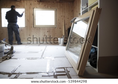 Worker in the background installing new, three pane wooden windows in an old wooden house, with a new window in the foreground. Home renovation, sustainable living, energy efficiency concept. 
 Royalty-Free Stock Photo #539844298