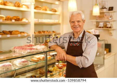 His hobby became his career. Happy senior man smiling leaning on the showcase while working at his own bakery running his small business copyspace