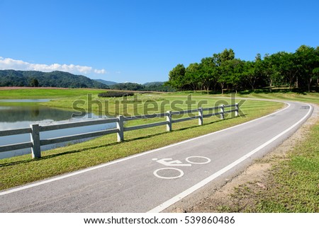 Scenery bicycle lane in  lake park with blue sky and mountain forest background.