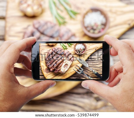 Taking photo of beef steak by smartphone. Closeup view of  process. File contains clipping paths for smartphone and hands and  picture on it.
