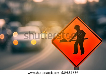 Construction warning sign on blur traffic road with colorful bokeh light abstract background. Copy space of transportation and travel concept. Retro tone filter effect color style.