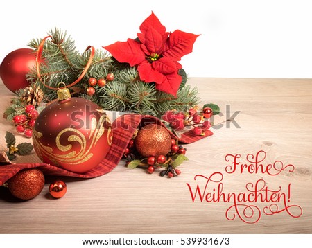 Wooden background with poinsettia and decorated Christmas tree twigs, text on the picture means "Merry Christmas" in German.