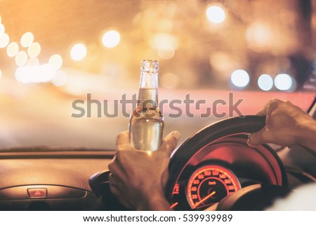 Drunk young man drives a car with a bottle of beer.  This is a campaign picture of "Don't Drink for Drive." Selective focus