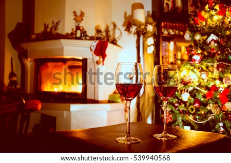 Two glasses with red wine on table. Blurred Christmas tree and fireplace in background.